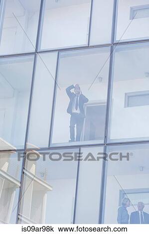 Businessman looking through window of glass fronted hotel whilst talking on smartphone View Large Photo Image Stock Image - Businessman looking through window of glass fronted hotel whilst talking on smartphone. Fotosearch