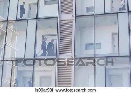 Stock Image - Businessmen and women in corridors of glass fronted hotel. Fotosearch