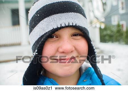 Stock Image - Close up portrait of girl wearing black and white striped hat in snowy garden. Fotosearch