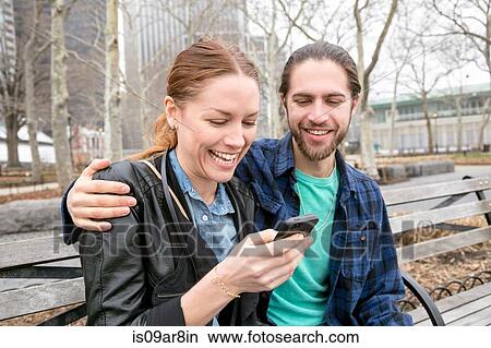 Couple checking messages on park bench, New York, New York, USA View Large Photo Image Picture - Couple checking messages on park bench, New York, New York, USA. Fotosearch
