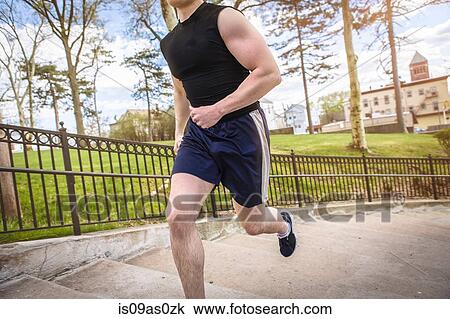 Stock Image - Cropped view of young male runner running up park stairway. Fotosearch