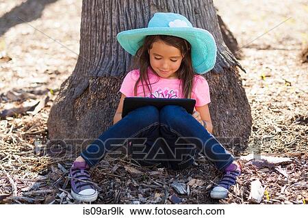 Cute girl leaning against tree trunk using digital tablet View Large Photo Image Stock Image - Cute girl leaning against tree trunk using digital tablet. Fotosearch