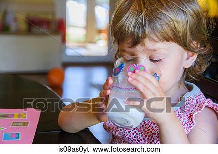 Stock Photograph - Cute young girl drinking glass of milk at kitchen table. Fotosearch
