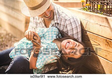Stock Image - Father tickling daughter in community garden. Fotosearch