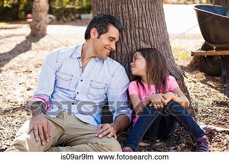 Picture - Girl and father leaning against tree in community garden. Fotosearch