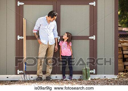 Stock Image - Girl looking at father in front of community garden shed. Fotosearch