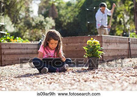 Stock Image - Girl sitting cross legged using digital tablet in community garden. Fotosearch