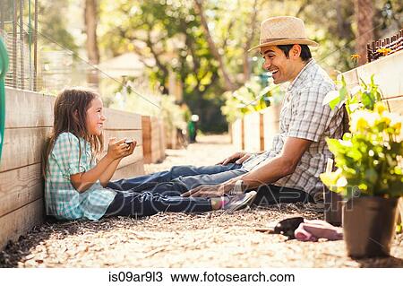 Stock Image - Girl using fathers smartphone in community garden. Fotosearch