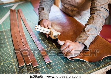 Stock Image - Hands of leather craftsman using wooden clamp on workshop bench. Fotosearch