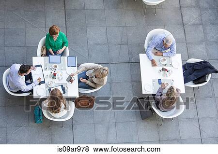 Stock Photo - High angle view of businessmen and businesswomen having working lunch on hotel terrace. Fotosearch