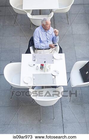 Stock Image - High angle view of senior businessman sitting at table on hotel terrace. Fotosearch