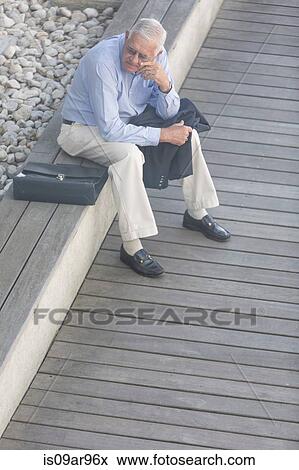 Stock Photo - High angle view of senior businessman sitting alone on hotel terrace. Fotosearch