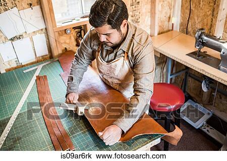 Stock Image - Leather craftsman using wooden clamp on workshop bench. Fotosearch