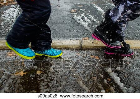 Stock Photograph - Legs of two girls wearing rubber boots crossing road. Fotosearch