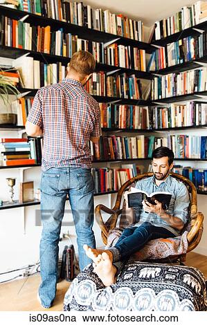 Male couple at home, reading and looking at books on bookshelf View Large Photo Image Stock Image - Male couple at home, reading and looking at books on bookshelf. Fotosearch