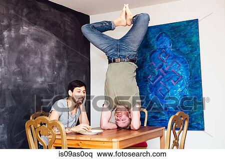 Male couple at home, young man eating meal whilst his partner does headstand on table View Large Photo Image Stock Photography - Male couple at home, young man eating meal whilst his partner does headstand on table. Fotosearch