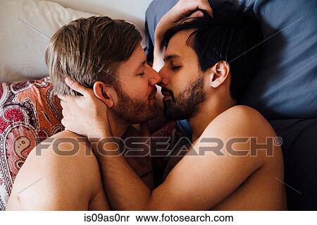 Stock Photography - Male couple, bare chested, lying on bed, kissing. Fotosearch