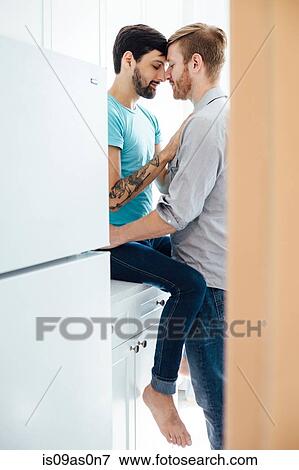 Stock Photo - Male couple in kitchen, face to face, embracing. Fotosearch