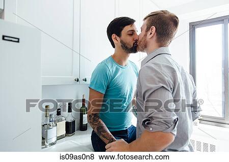 Stock Photo - Male couple kissing in kitchen. Fotosearch