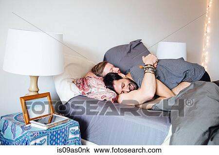 Stock Image - Male couple on bed, embracing, smiling. Fotosearch