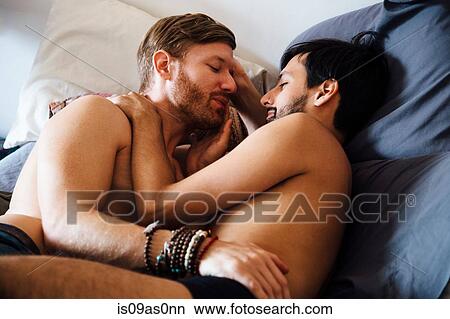 Picture - Male couple, partially dressed, lying on bed, embracing. Fotosearch