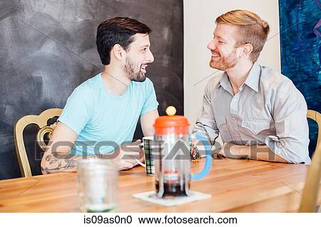 Stock Image - Male couple sitting at table, drinking coffee. Fotosearch
