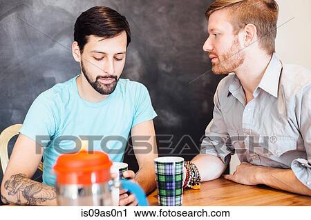 Stock Image - Male couple sitting at table, drinking coffee. Fotosearch