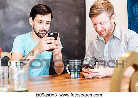 Male couple sitting at table, having coffee, looking at smartphones View Large Photo Image Stock Image - Male couple sitting at table, having coffee, looking at smartphones. Fotosearch