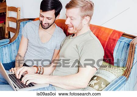 Male couple sitting on sofa, looking at laptop, smiling View Large Photo Image Stock Image - Male couple sitting on sofa, looking at laptop, smiling. Fotosearch