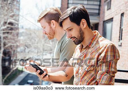 Male couple standing on balcony, looking at smartphones View Large Photo Image Stock Image - Male couple standing on balcony, looking at smartphones. Fotosearch