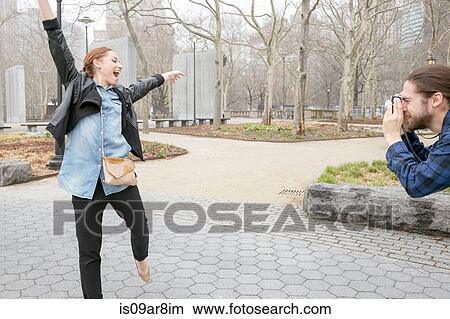 Picture - Man taking photograph of girlfriend in park, New York, New York, USA. Fotosearch