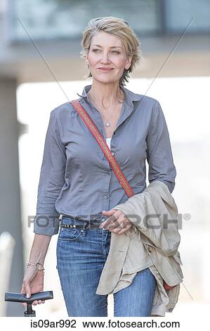 Mature woman leaving hotel with wheeled suitcase View Large Photo Image Stock Image - Mature woman leaving hotel with wheeled suitcase. Fotosearch