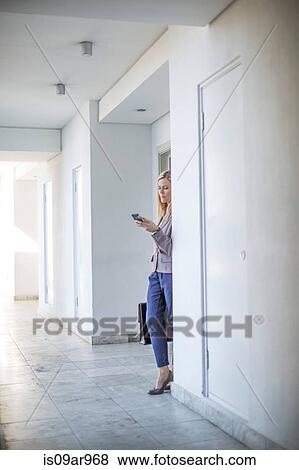 Mid adult businesswoman reading smartphone text in hotel corridor View Large Photo Image Stock Photo - Mid adult businesswoman reading smartphone text in hotel corridor. Fotosearch