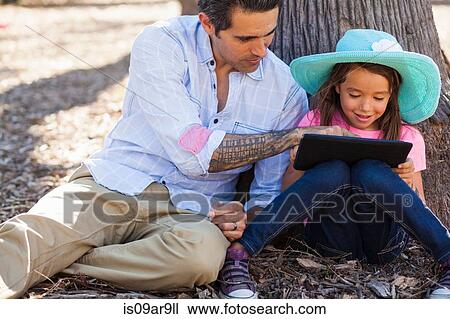 Mid adult man and daughter leaning against tree using digital tablet View Large Photo Image Stock Image - Mid adult man and daughter leaning against tree using digital tablet. Fotosearch