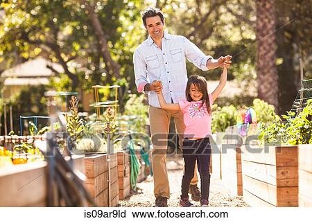 Mid adult man holding hands with daughter in community garden View Large Photo Image Stock Image - Mid adult man holding hands with daughter in community garden. Fotosearch