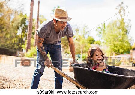 Mid adult man in community garden pushing daughter in wheelbarrow View Large Photo Image Stock Image - Mid adult man in community garden pushing daughter in wheelbarrow. Fotosearch