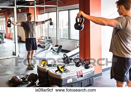 Mid adult man looking at himself in gym mirror training with kettle bells View Large Photo Image Stock Image - Mid adult man looking at himself in gym mirror training with kettle bells. Fotosearch