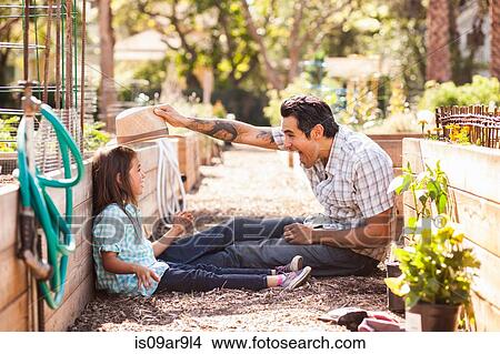 Mid adult man putting fedora on daughter in community garden View Large Photo Image Picture - Mid adult man putting fedora on daughter in community garden. Fotosearch