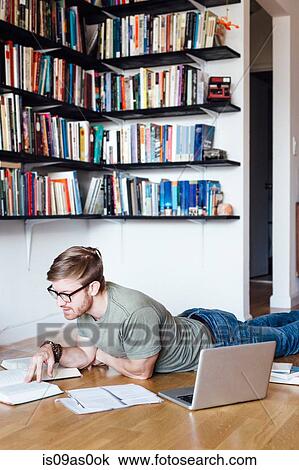 Mid adult man sitting lying on floor, looking through books View Large Photo Image Stock Image - Mid adult man sitting lying on floor, looking through books. Fotosearch