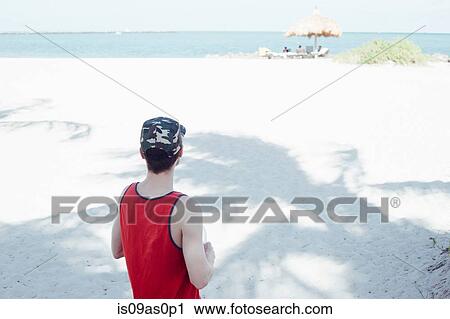 Stock Image - Mid adult man, standing on beach, looking at view, rear view, Miami Beach, Florida, USA. Fotosearch