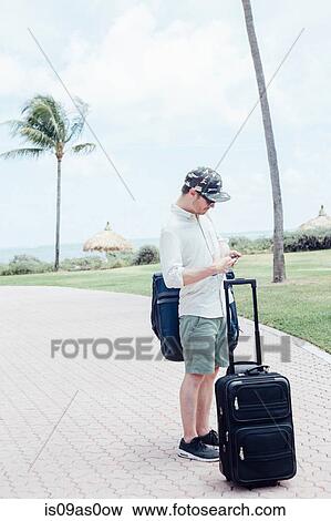 Mid adult man standing with suitcases, looking at smartphone, Miami Beach, Florida, USA View Large Photo Image Stock Photo - Mid adult man standing with suitcases, looking at smartphone, Miami Beach, Florida, USA. Fotosearch