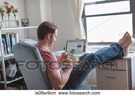 Mid adult man with feet up on desk reading smartphone texts View Large Photo Image Picture - Mid adult man with feet up on desk reading smartphone texts. Fotosearch