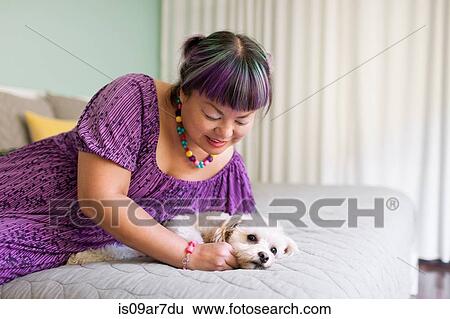 Stock Photograph - Mid adult woman lying on bed with dog. Fotosearch