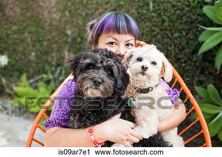 Stock Image - Mid adult woman sitting outdoors, hugging two dogs. Fotosearch