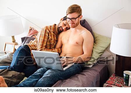 Mid couple relaxing on bed together, looking at laptop screen View Large Photo Image Stock Photo - Mid couple relaxing on bed together, looking at laptop screen. Fotosearch