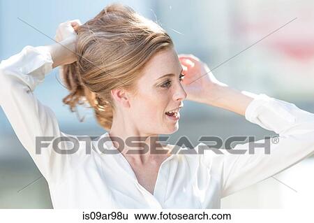 Stock Photograph - Portrait of beautiful young woman with hands holding back long red hair. Fotosearch