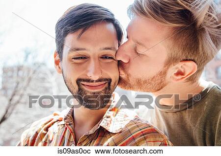 Stock Image - Portrait of male couple, mid adult man kissing his partner's cheek. Fotosearch