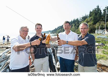 Stock Photography - Portrait of mature men and son toasting each other with bottled beer on beach. Fotosearch