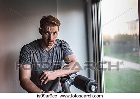 Stock Image - Portrait of sweaty mid adult man leaning on exercise machine in gym. Fotosearch