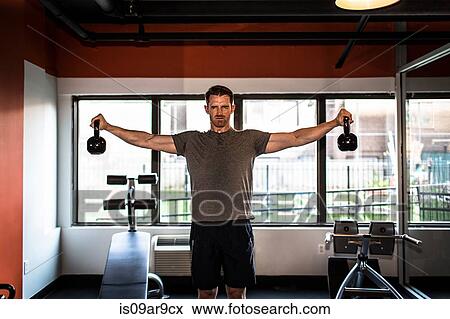 Stock Photo - Portrait of sweaty mid adult man weight training with kettle bells. Fotosearch